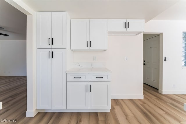 kitchen featuring light stone countertops, white cabinets, and light wood-type flooring