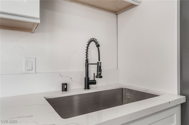 room details with white cabinetry, sink, and light stone counters