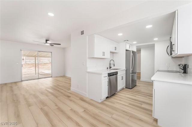 kitchen with sink, light wood-type flooring, ceiling fan, stainless steel appliances, and white cabinets