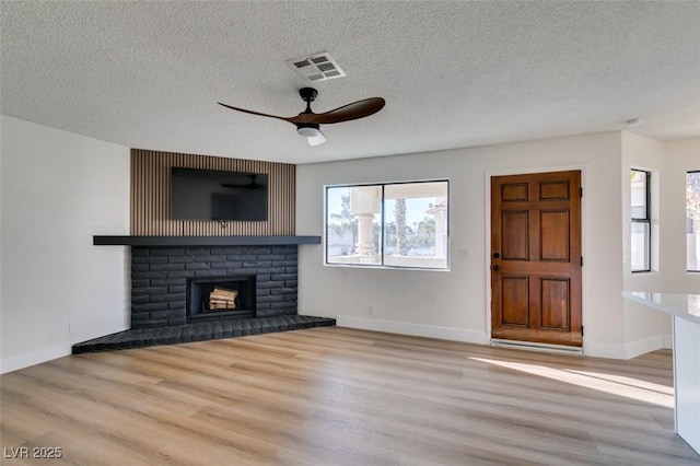 unfurnished living room with a fireplace, wood finished floors, visible vents, and a textured ceiling