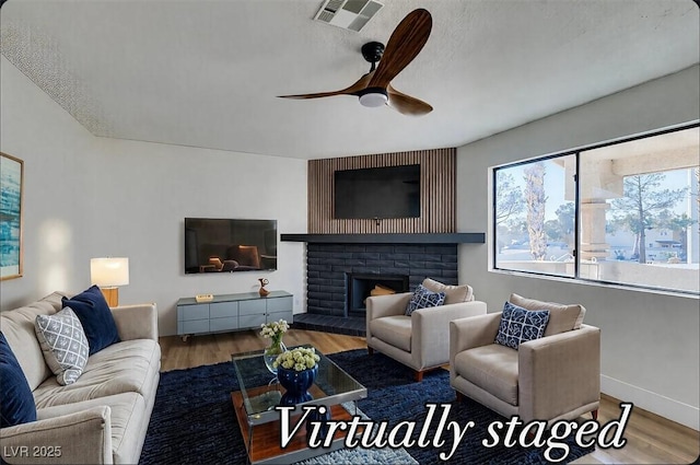 living room with a ceiling fan, wood finished floors, visible vents, and a fireplace