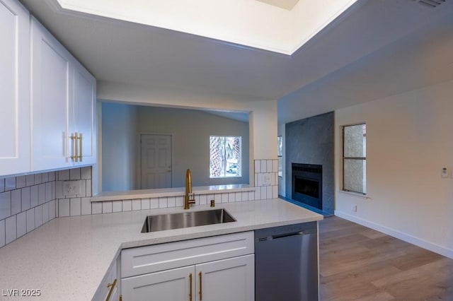 kitchen featuring dishwashing machine, sink, white cabinetry, and kitchen peninsula