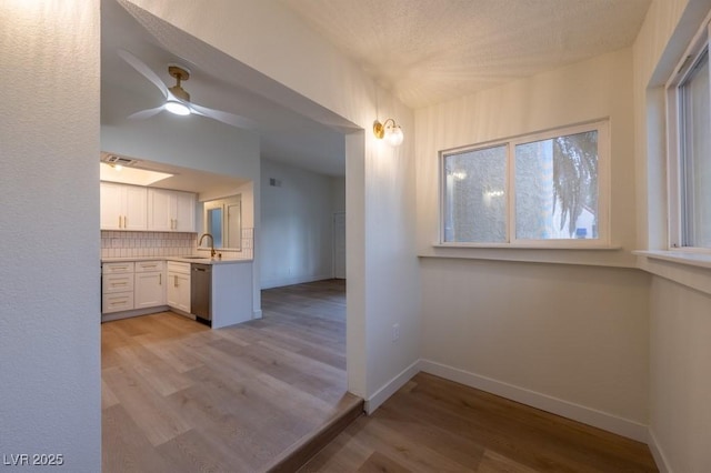 kitchen with sink, white cabinets, decorative backsplash, stainless steel dishwasher, and light wood-type flooring