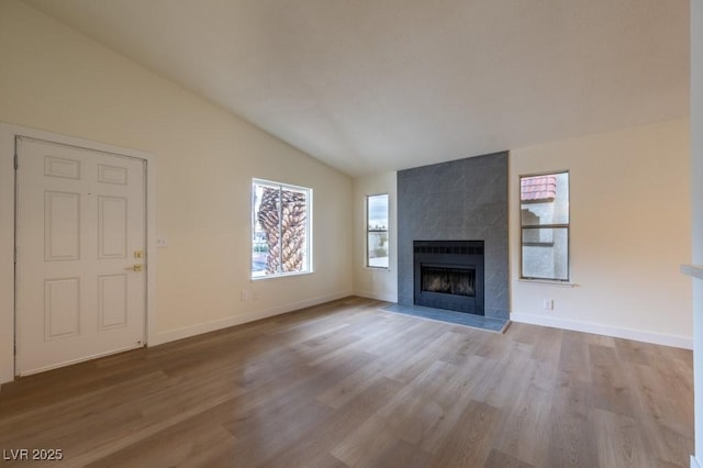 unfurnished living room featuring a tiled fireplace, vaulted ceiling, and light hardwood / wood-style flooring