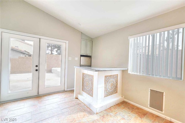 interior space featuring baseboards, lofted ceiling, stone finish flooring, light countertops, and french doors