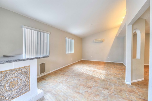 unfurnished living room with vaulted ceiling, a wall unit AC, visible vents, and baseboards