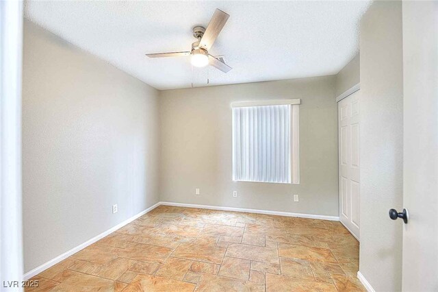 empty room featuring ceiling fan, baseboards, a textured ceiling, and stone finish flooring