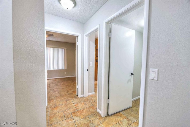 hallway featuring a textured ceiling, stone finish flooring, a textured wall, and baseboards