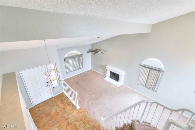 interior space featuring carpet floors, a fireplace, stairway, a textured ceiling, and ceiling fan with notable chandelier