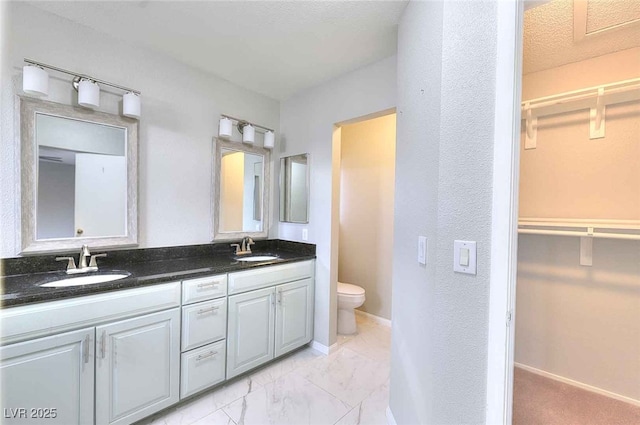 full bath featuring toilet, marble finish floor, double vanity, and a sink