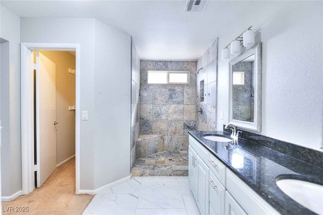 full bath with marble finish floor, double vanity, visible vents, a sink, and a tile shower