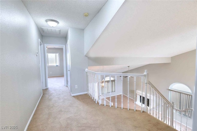 hallway with carpet, visible vents, a textured ceiling, an upstairs landing, and baseboards