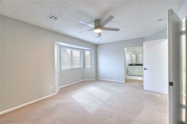 unfurnished bedroom featuring a textured ceiling, connected bathroom, light carpet, visible vents, and baseboards