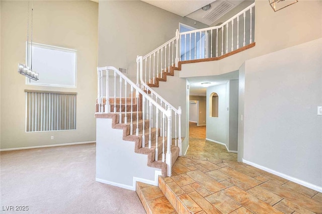 stairs with visible vents, baseboards, arched walkways, a high ceiling, and carpet floors