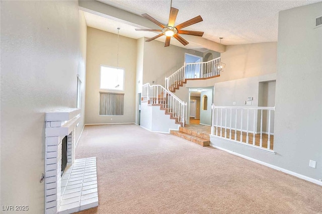 unfurnished living room with stairs, a textured ceiling, a brick fireplace, and carpet flooring