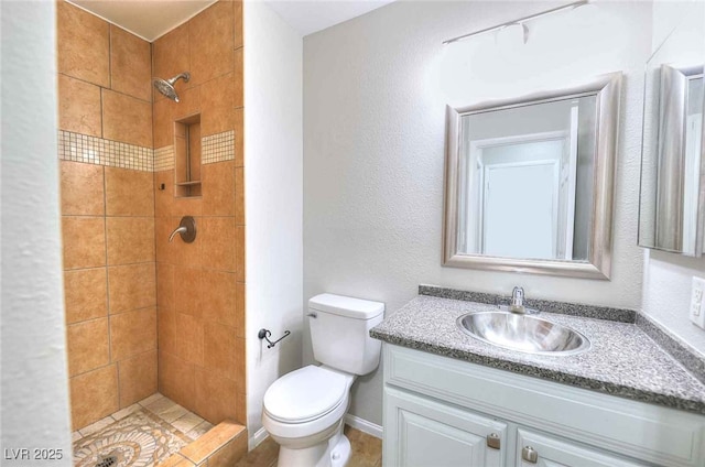 bathroom featuring a textured wall, toilet, vanity, tiled shower, and baseboards