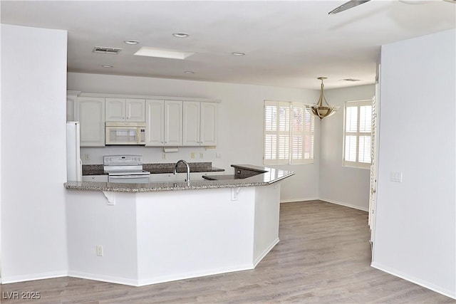 kitchen featuring hanging light fixtures, kitchen peninsula, white appliances, dark stone counters, and white cabinets