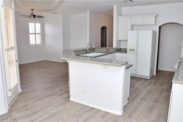 kitchen with sink, white cabinetry, white refrigerator with ice dispenser, kitchen peninsula, and light stone countertops