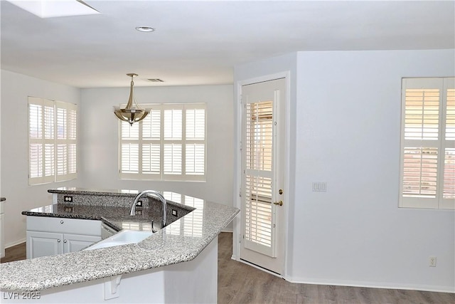 kitchen featuring pendant lighting, sink, white cabinetry, light stone counters, and a healthy amount of sunlight