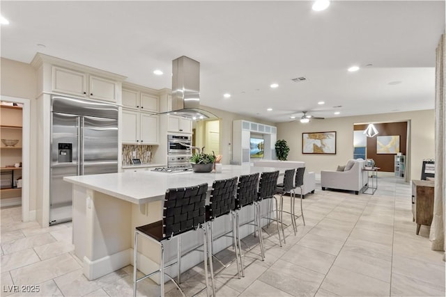 kitchen featuring island range hood, a kitchen breakfast bar, decorative backsplash, built in refrigerator, and a large island