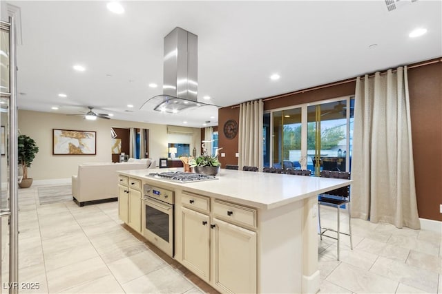 kitchen with a kitchen island, appliances with stainless steel finishes, island range hood, a kitchen bar, and cream cabinets