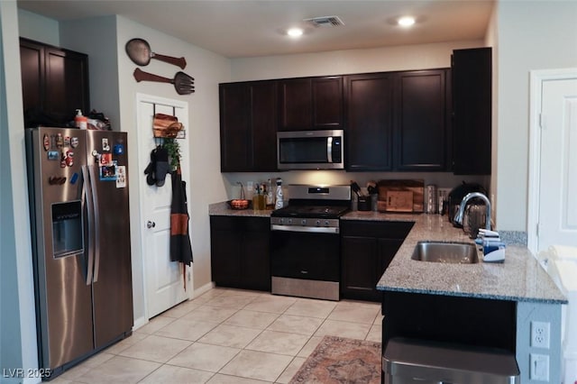 kitchen with sink, dark brown cabinets, light tile patterned floors, stainless steel appliances, and light stone countertops