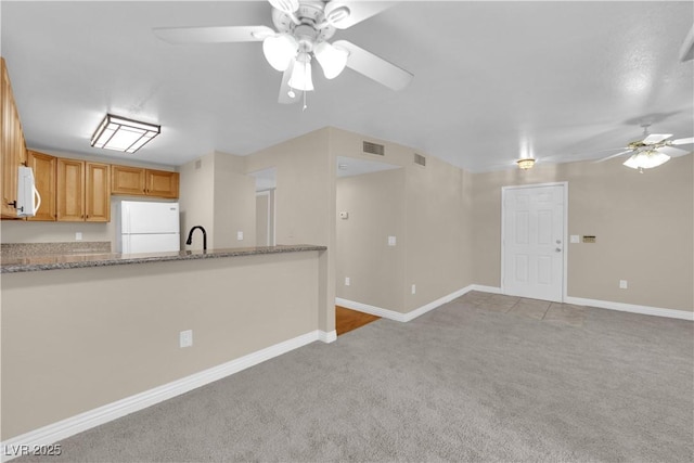 kitchen with sink, white appliances, ceiling fan, light stone countertops, and light carpet