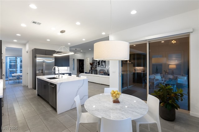 kitchen featuring decorative light fixtures, sink, light tile patterned floors, stainless steel appliances, and a center island with sink