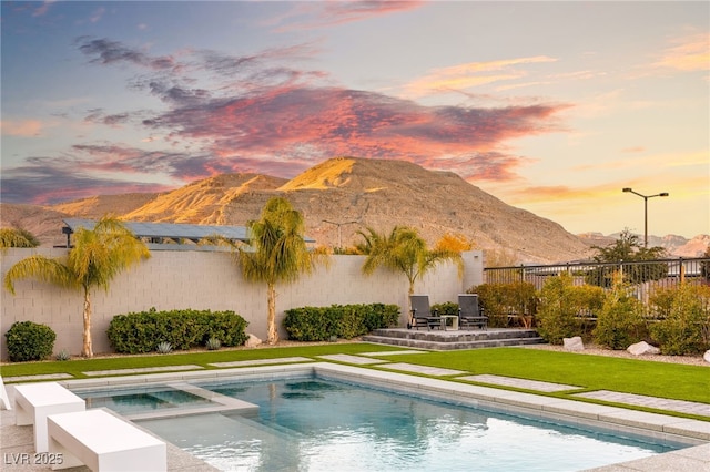 pool at dusk featuring an in ground hot tub, a mountain view, and a lawn