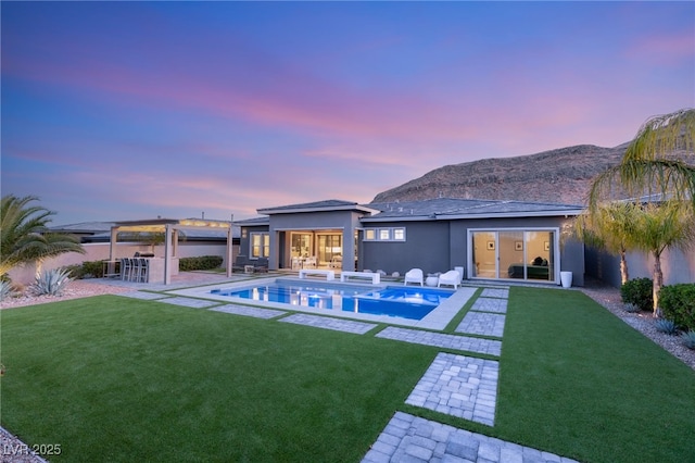 pool at dusk with a mountain view, a yard, and a patio area