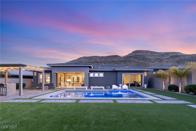 back house at dusk featuring a mountain view, a yard, and a patio