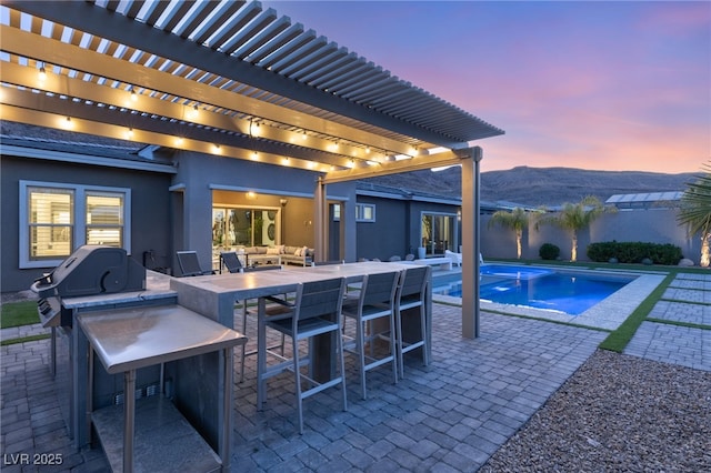 pool at dusk with grilling area, outdoor lounge area, a pergola, an outdoor bar, and a mountain view