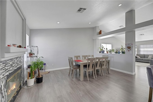 dining area with wood-type flooring, vaulted ceiling, a tile fireplace, and a wealth of natural light