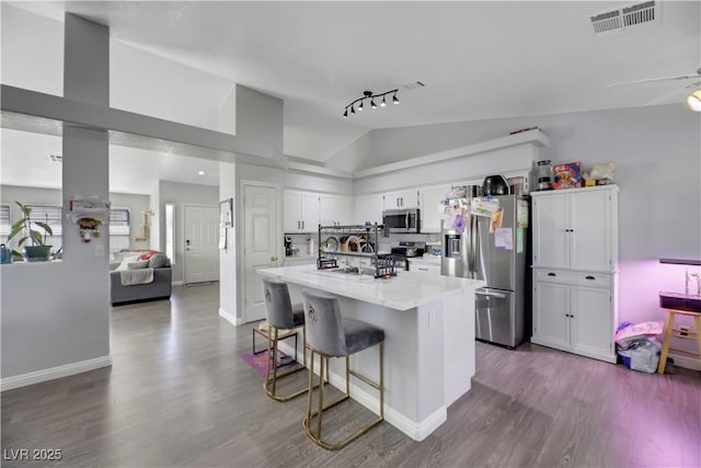 kitchen with lofted ceiling, a breakfast bar area, wood-type flooring, appliances with stainless steel finishes, and white cabinets