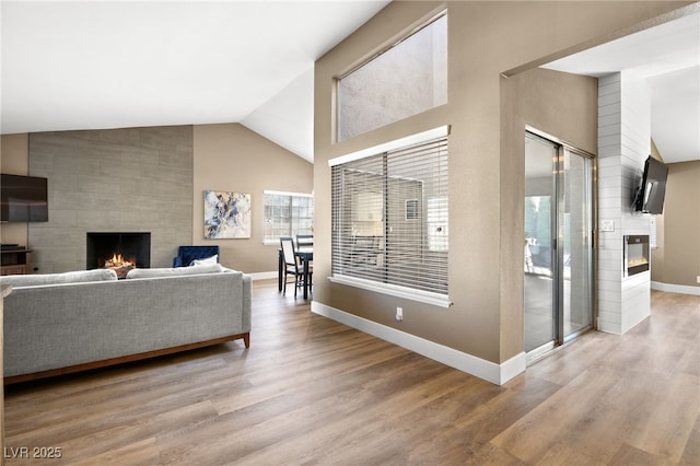 living room with high vaulted ceiling, a tile fireplace, and light hardwood / wood-style flooring