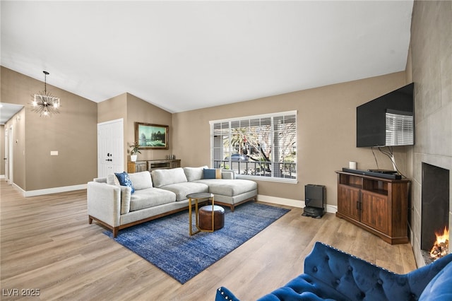 living room featuring vaulted ceiling, a large fireplace, an inviting chandelier, and light hardwood / wood-style floors