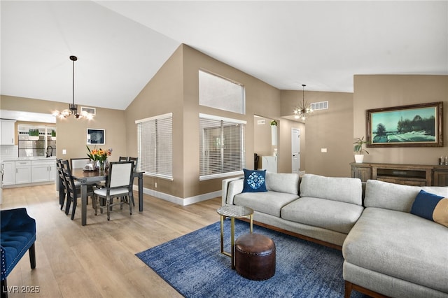 living room with high vaulted ceiling, light wood-type flooring, and a notable chandelier