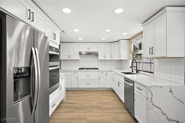 kitchen with sink, light hardwood / wood-style flooring, stainless steel appliances, light stone counters, and white cabinets