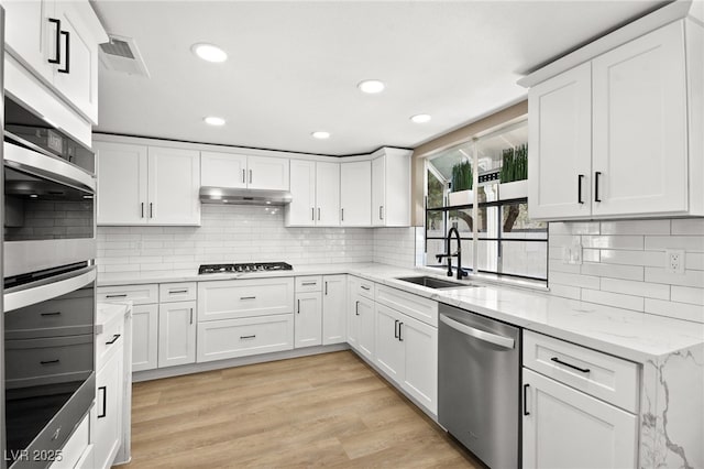 kitchen featuring sink, white cabinets, light hardwood / wood-style floors, stainless steel appliances, and light stone countertops