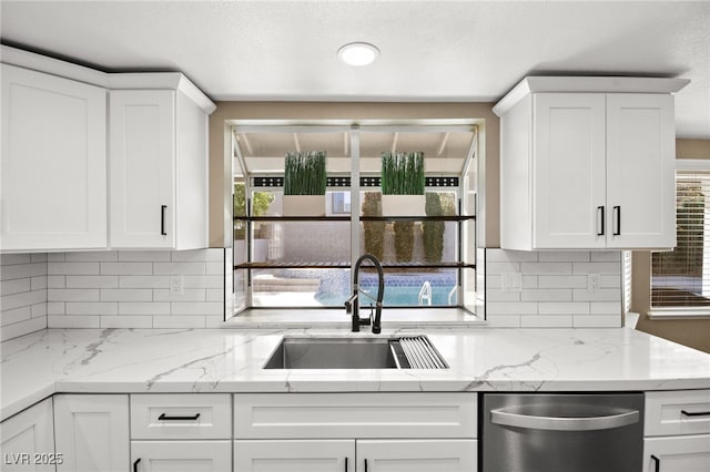 kitchen featuring white cabinetry, sink, backsplash, stainless steel dishwasher, and light stone countertops