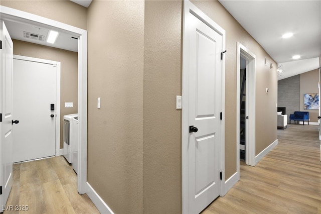 hallway with independent washer and dryer and light hardwood / wood-style flooring