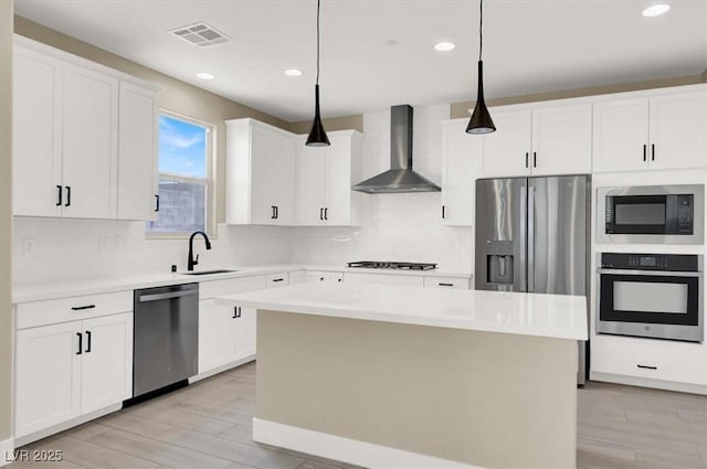 kitchen with sink, stainless steel appliances, a center island, decorative light fixtures, and wall chimney exhaust hood