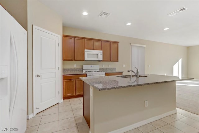 kitchen featuring sink, white appliances, light tile patterned floors, and a center island with sink