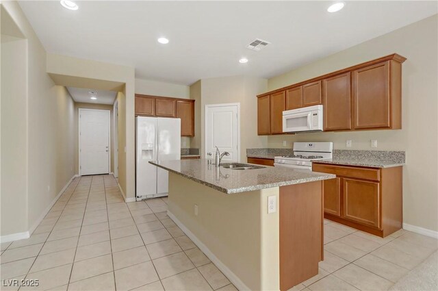 kitchen with sink, white appliances, light tile patterned floors, a kitchen island with sink, and light stone countertops