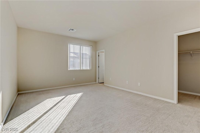 unfurnished bedroom with a walk in closet, a closet, and light carpet