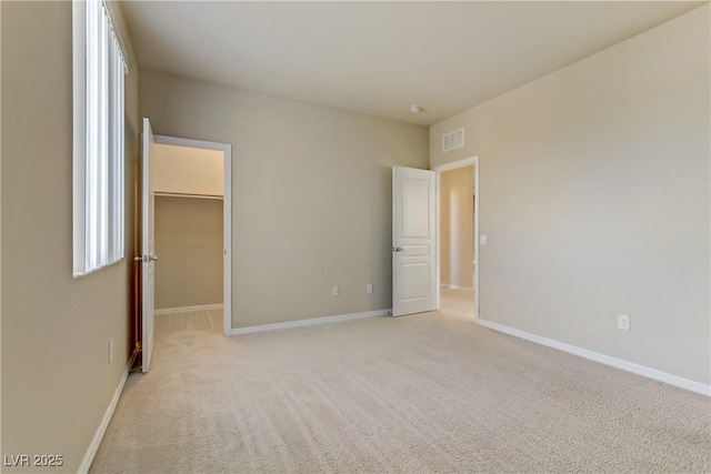 unfurnished bedroom with light carpet, a spacious closet, and a closet