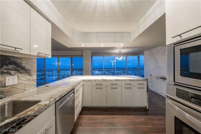 kitchen with dark wood-type flooring, white cabinetry, a tray ceiling, kitchen peninsula, and stainless steel appliances