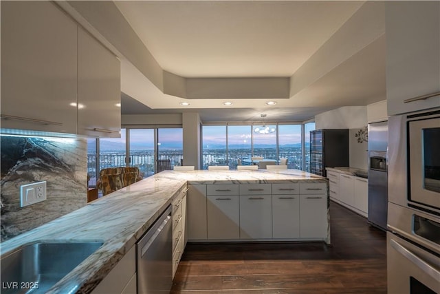 kitchen with white cabinetry, light stone counters, dark hardwood / wood-style floors, kitchen peninsula, and stainless steel appliances