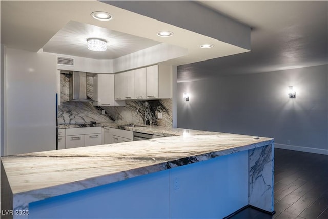 kitchen with white cabinetry, sink, backsplash, kitchen peninsula, and wall chimney exhaust hood