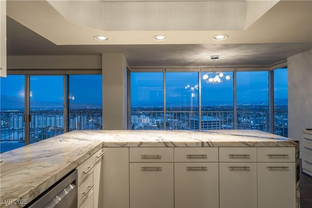 kitchen featuring light stone counters, hanging light fixtures, stainless steel dishwasher, and white cabinets